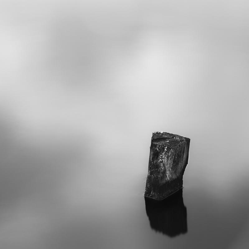 Dipping into my reflection - Minimalistic long exposure.  Part of an old pier structure rising from the water surface.